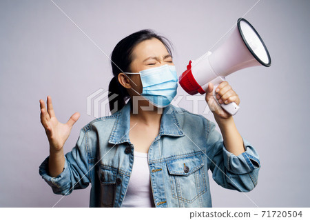 Asian woman wearing protective face mask shouting with megaphone isolated over white background. Asian woman wearing protective face mask shouting with megaphone isolated over white background. 71720504