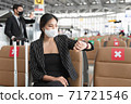 Young businesswoman wearing face mask sitting at the airport and looking on her watch to check time to on board. 71721546