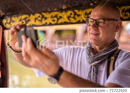 Face of happy senior tourist man taking picture with phone while spending vacation in Ayutthaya 71722920