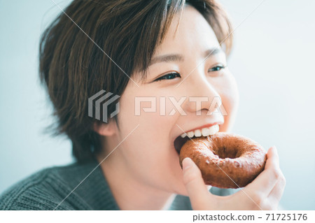 Woman in her 30s eating a donut 71725176