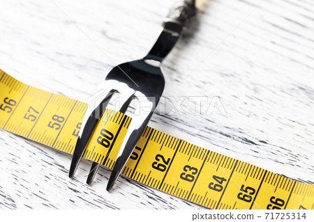 Yellow centimeter wrapped dessert fork on an old wooden table with the number 60. The concept of restriction in food for a slim figure with parameters 36 24 36 or 90 60 90 Yellow centimeter wrapped dessert fork on an old wooden table with the number 60. The concept of restriction in food for a slim figure with parameters 36 24 36 or 90 60 90 71725314