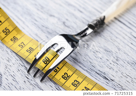 Yellow centimeter wrapped dessert fork on an old wooden table with the number 60. The concept of restriction in food for a slim figure with parameters 36 24 36 or 90 60 90 Yellow centimeter wrapped dessert fork on an old wooden table with the number 60. The concept of restriction in food for a slim figure with parameters 36 24 36 or 90 60 90 71725315