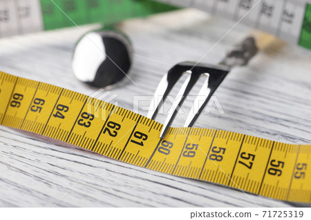 A multi-colored centimeter wrapped a dessert fork on an old wooden table showing the number 60. The concept of dietary nutrition to maintain a slim figure with parameters 36 24 36 or 90 60 90 A multi-colored centimeter wrapped a dessert fork on an old wooden table showing the number 60. The concept of dietary nutrition to maintain a slim figure with parameters 36 24 36 or 90 60 90 71725319