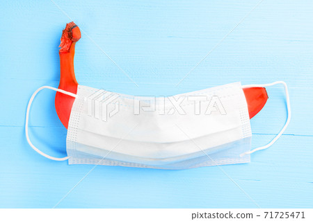 Red banana covered with medical protective mask on a wooden light blue background. The concept of sexual problems and sexually transmitted infections 71725471