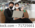 Businesswoman wearing face mask having gesture hand at laptop to say good bye with colleague at the other side of video conference after online meeting finished. 71725661