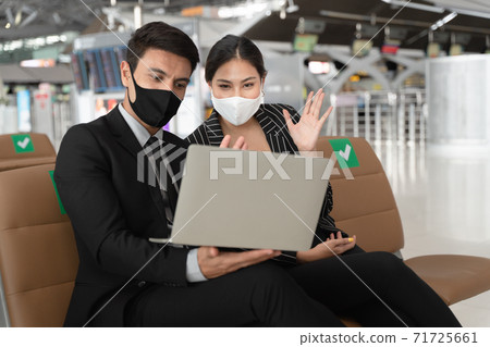 Businesswoman wearing face mask having gesture hand at laptop to say good bye with colleague at the other side of video conference after online meeting finished. 71725661
