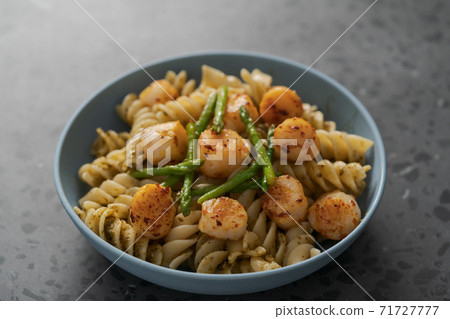 Fusilli pasta with scallops and asparagus in blue bowl on concrete surface 71727777