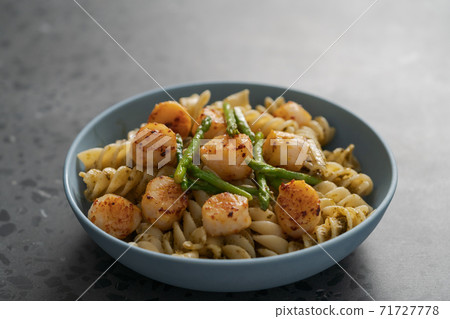 Fusilli pasta with scallops and asparagus in blue bowl on concrete surface Fusilli pasta with scallops and asparagus in blue bowl on concrete surface 71727778