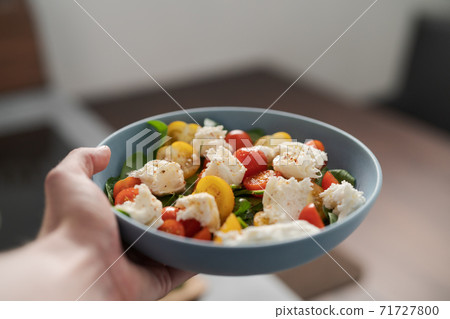 amn hand hold salad with red and yellow cherry tomatoes , mozzarella and spinach in blue bowl amn hand hold salad with red and yellow cherry tomatoes , mozzarella and spinach in blue bowl 71727800