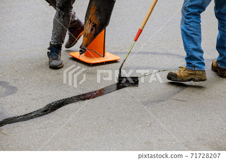 Road surface restoration work in the worker performs on road patcher work on the repair of cracks by filling and sealing with coated by bitumen emulsion Road surface restoration work in the worker performs on road patcher work on the repair of cracks by filling and sealing with coated by bitumen emulsion 71728207