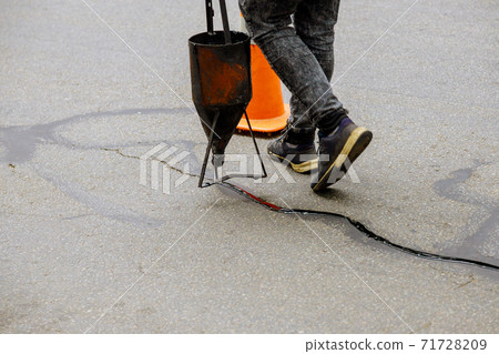 Sealing joint crack in asphalt road surface restoration work. 71728209