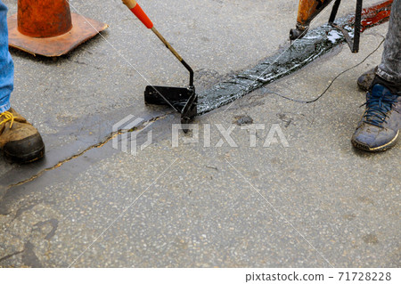 Road surface restoration work in the worker performs on road patcher work on the repair of cracks by filling and sealing with coated by bitumen emulsion 71728228