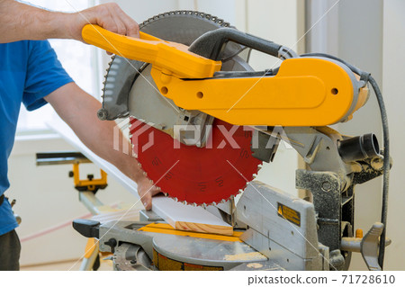 Worker cuts wood baseboard on the power miter saw new home Worker cuts wood baseboard on the power miter saw new home 71728610