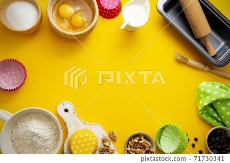 Baking frame with flour, sugar, milk, eggs, wallnuts, chocolate chips, rolling pin, baking mold. Yellow background with copy space. Baking frame with flour, sugar, milk, eggs, wallnuts, chocolate chips, rolling pin, baking mold. Yellow background with copy space. 71730341
