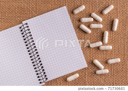 Medical capsules and pills around a blank notepad on a wicker background, close-up, top view, with copy space. 71730681