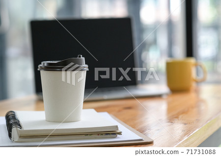 Close-up shot of White take away coffee cup place on a notebook in the office. 71731088