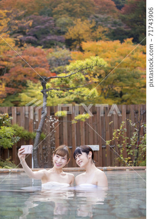 兩名年輕婦女在露天浴場拍照以秋葉為背景 兩名年輕婦女在露天浴場拍照以秋葉為背景 71743906
