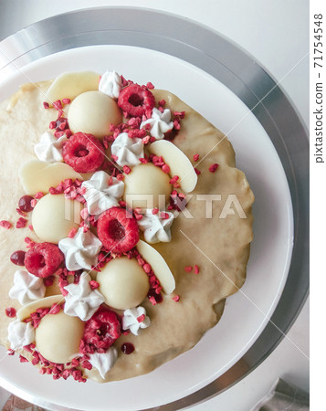 Raw vegan raspberry cake decorated with white chocolate and berries. Vegetarian top view cashew cream cheesecake gluten free. Lactose sugar free desert on white plate. Indoor photo Raw vegan raspberry cake decorated with white chocolate and berries. Vegetarian top view cashew cream cheesecake gluten free. Lactose sugar free desert on white plate. Indoor photo 71754548