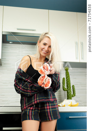 A woman in the kitchen in home clothes with a peeled pomelo fruit smiles A woman in the kitchen in home clothes with a peeled pomelo fruit smiles 71754838