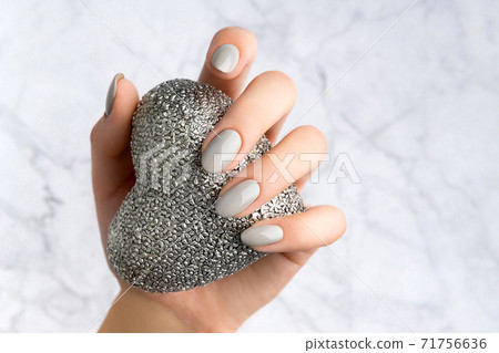 Beautiful womans hand with manicure holding silver heart 71756636