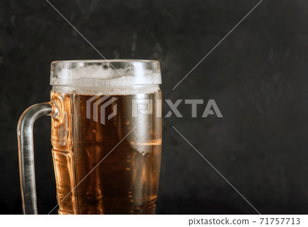 mug of light beer with foam on a dark background, alcoholic drink 71757713