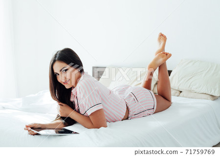 Beautiful woman in pajamas in the bedroom on the bed with an internet tablet Beautiful woman in pajamas in the bedroom on the bed with an internet tablet 71759769