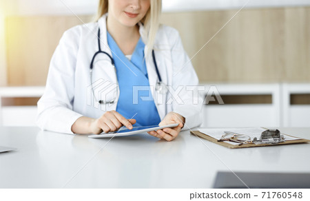 Unknown woman-doctor sitting in sunny clinic and using tablet pc, close-up. Data and best service in medicine Unknown woman-doctor sitting in sunny clinic and using tablet pc, close-up. Data and best service in medicine 71760548