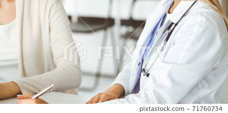 Unknown woman-doctor sitting and communicating with female patient. Physician checks medical history record and exam results, close-up. Healthcare concept 71760734