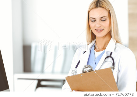 Doctor woman at work in hospital controls medication history records and exam results while using clipboard. Medicine and healthcare concept 71760778