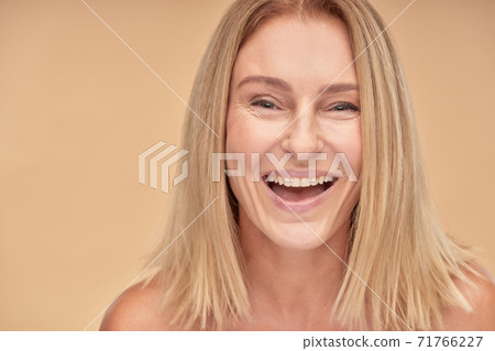 Portrait of attractive happy mature lady smiling at camera while posing over beige background in studio Portrait of attractive happy mature lady smiling at camera while posing over beige background in studio 71766227