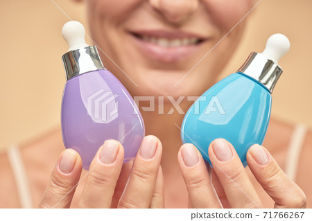 Close up of happy adult woman holding jars of serum to moisturize the skin Close up of happy adult woman holding jars of serum to moisturize the skin 71766267