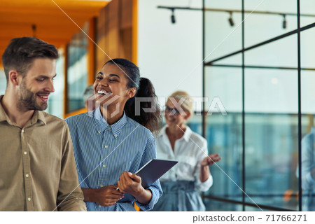 Two young cheerful diverse colleagues talking after business meeting while standing in the modern office or coworking space 71766271