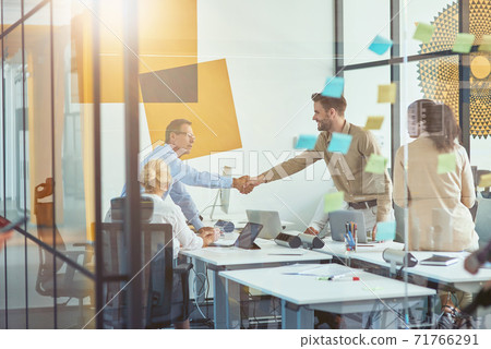 Good deal. Two businessmen or coworkers shaking hands while having a meeting with colleagues in the modern office 71766291