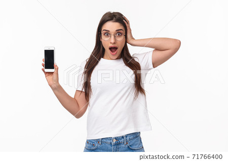 Communication, technology and lifestyle concept. Waist-up portrait of astonished surprised and excited young woman in glasses, gasping and touch head shocked as showing mobile phone awesome app Communication, technology and lifestyle concept. Waist-up portrait of astonished surprised and excited young woman in glasses, gasping and touch head shocked as showing mobile phone awesome app 71766400