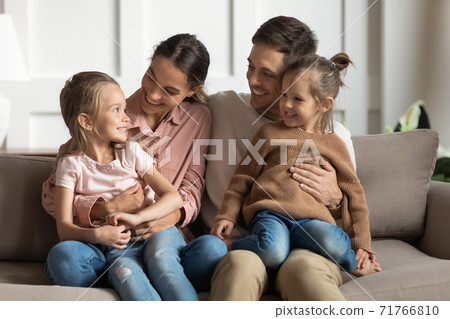 Little daughters sit on parents laps talking resting on couch 71766810