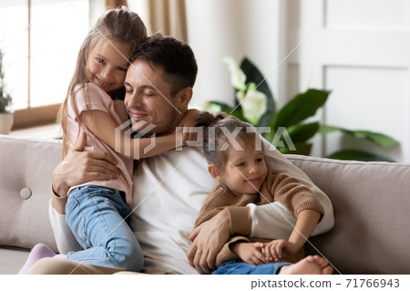 Dad hug two cute daughters resting together on couch Dad hug two cute daughters resting together on couch 71766943