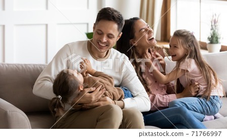 Parents play with daughters sit on couch in living room Parents play with daughters sit on couch in living room 71766997