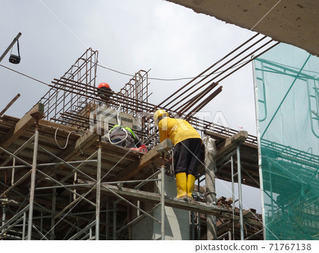 MALACCA, MALAYSIA -MARCH 2, 2020: Construction workers working at height install reinforcement bars at the construction site. They are supplied with harnesses and other safety equipment. 71767138