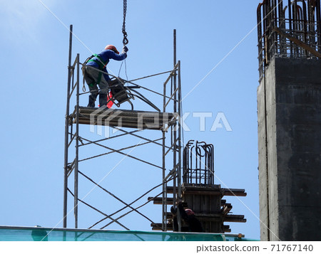 MALACCA, MALAYSIA -MARCH 2, 2020: Construction workers working at height install reinforcement bars at the construction site. They are supplied with harnesses and other safety equipment. MALACCA, MALAYSIA -MARCH 2, 2020: Construction workers working at height install reinforcement bars at the construction site. They are supplied with harnesses and other safety equipment. 71767140