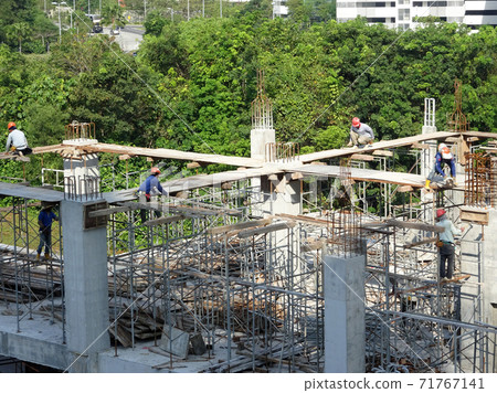 MALACCA, MALAYSIA -MARCH 2, 2020: Construction workers working at height install reinforcement bars at the construction site. They are supplied with harnesses and other safety equipment. MALACCA, MALAYSIA -MARCH 2, 2020: Construction workers working at height install reinforcement bars at the construction site. They are supplied with harnesses and other safety equipment. 71767141