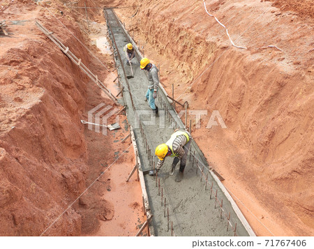 KUALA LUMPUR, MALAYSIA - November 20, 2020: Construction workers are levelling a layer of lean concrete in the trenches at the construction site. Lean concrete is poured from the truck. KUALA LUMPUR, MALAYSIA - November 20, 2020: Construction workers are levelling a layer of lean concrete in the trenches at the construction site. Lean concrete is poured from the truck. 71767406