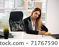 Portrait of cheerful businesswoman writing on contract sitting at desk in office. The concept of profession and leisure 71767590