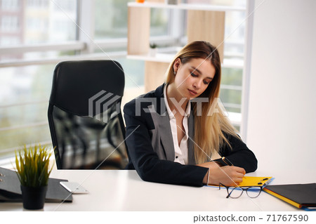 Portrait of cheerful businesswoman writing on contract sitting at desk in office. The concept of profession and leisure 71767590