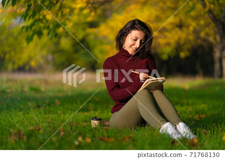 A person write notes sitting on a lawn in an autumn park. Joyful state of mind. Looking for inspiration A person write notes sitting on a lawn in an autumn park. Joyful state of mind. Looking for inspiration 71768130