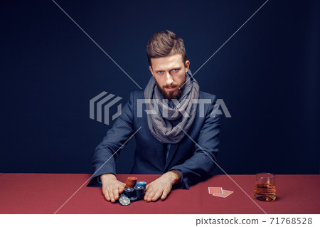 Stylish bearded Man in suit and scarf playing in dark casino, smoking cigar, drink whiskey Stylish bearded Man in suit and scarf playing in dark casino, smoking cigar, drink whiskey 71768528