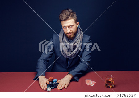 Stylish bearded Man in suit and scarf playing in dark casino, smoking cigar, drink whiskey Stylish bearded Man in suit and scarf playing in dark casino, smoking cigar, drink whiskey 71768537