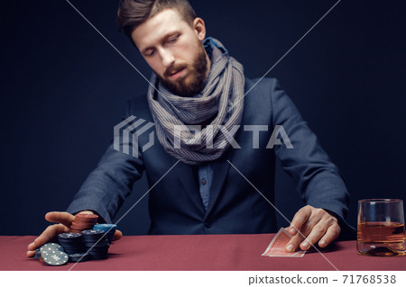 Stylish bearded Man in suit and scarf playing in dark casino, smoking cigar, drink whiskey Stylish bearded Man in suit and scarf playing in dark casino, smoking cigar, drink whiskey 71768538