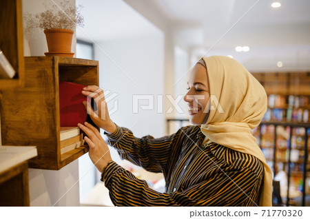 Smiling arab girl in hijab at the bookshelf Smiling arab girl in hijab at the bookshelf 71770320