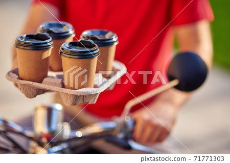 Male courier holding four coffee cups, delivering order by scooter to customer 71771303