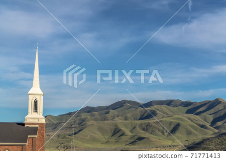 Rooftop and steeple of a church against power lines mountain and blue sky Rooftop and steeple of a church against power lines mountain and blue sky 71771413